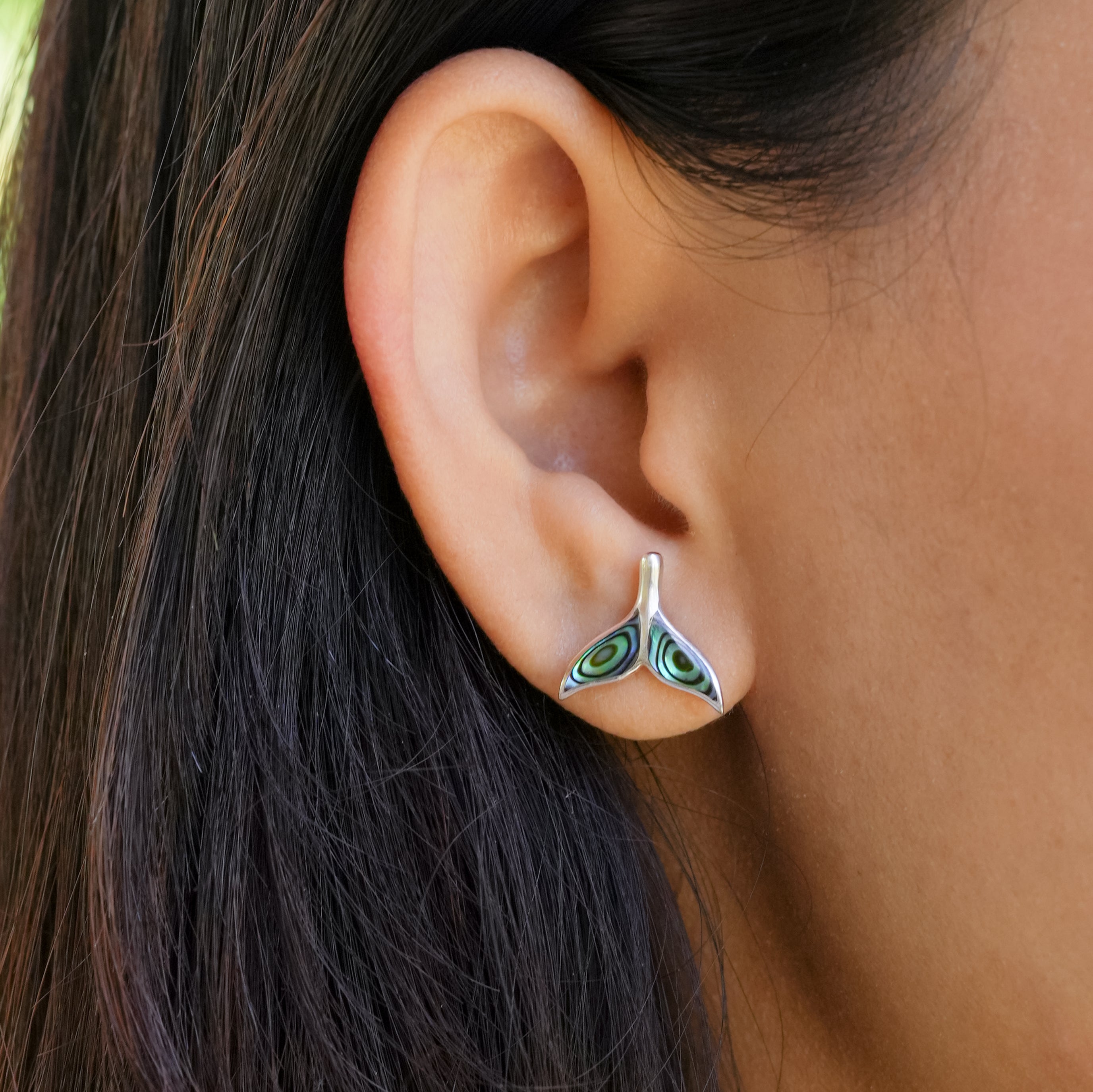 Close‑up image showing one whale‑tail‑shaped Abalone Shell stud earring worn on a person’s ear to display scale.