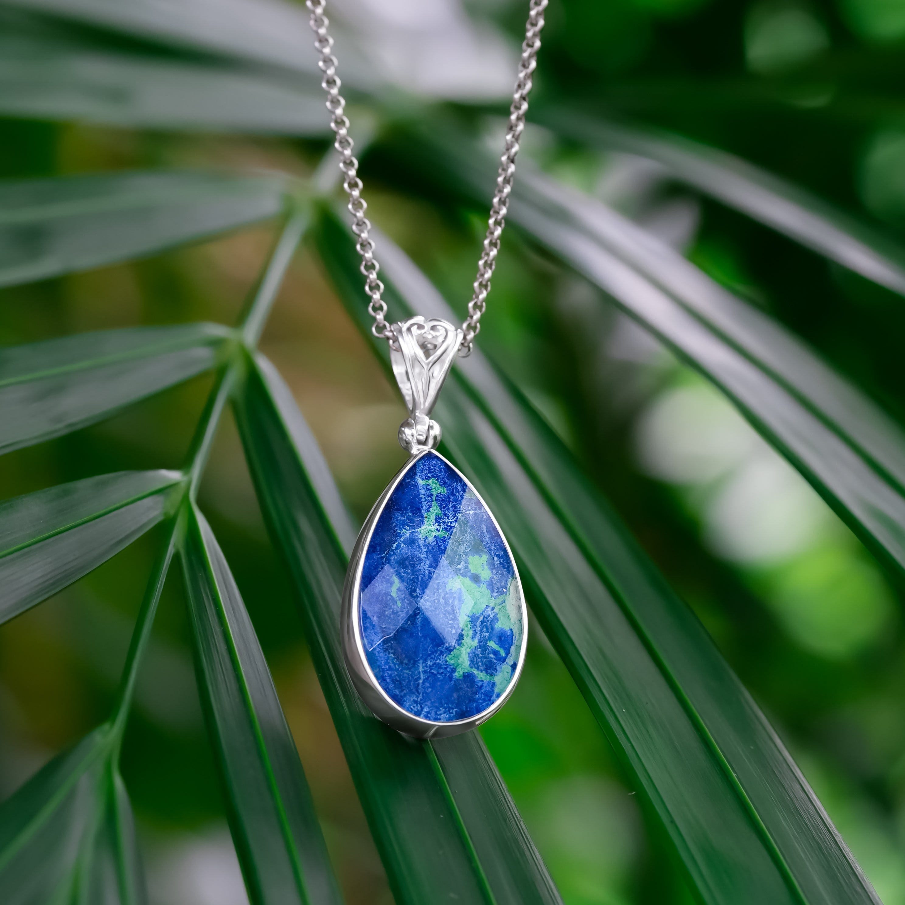 Angled view of a faceted azurite malachite pear pendant set in sterling silver, showing blue and green color variation while hanging from a chain