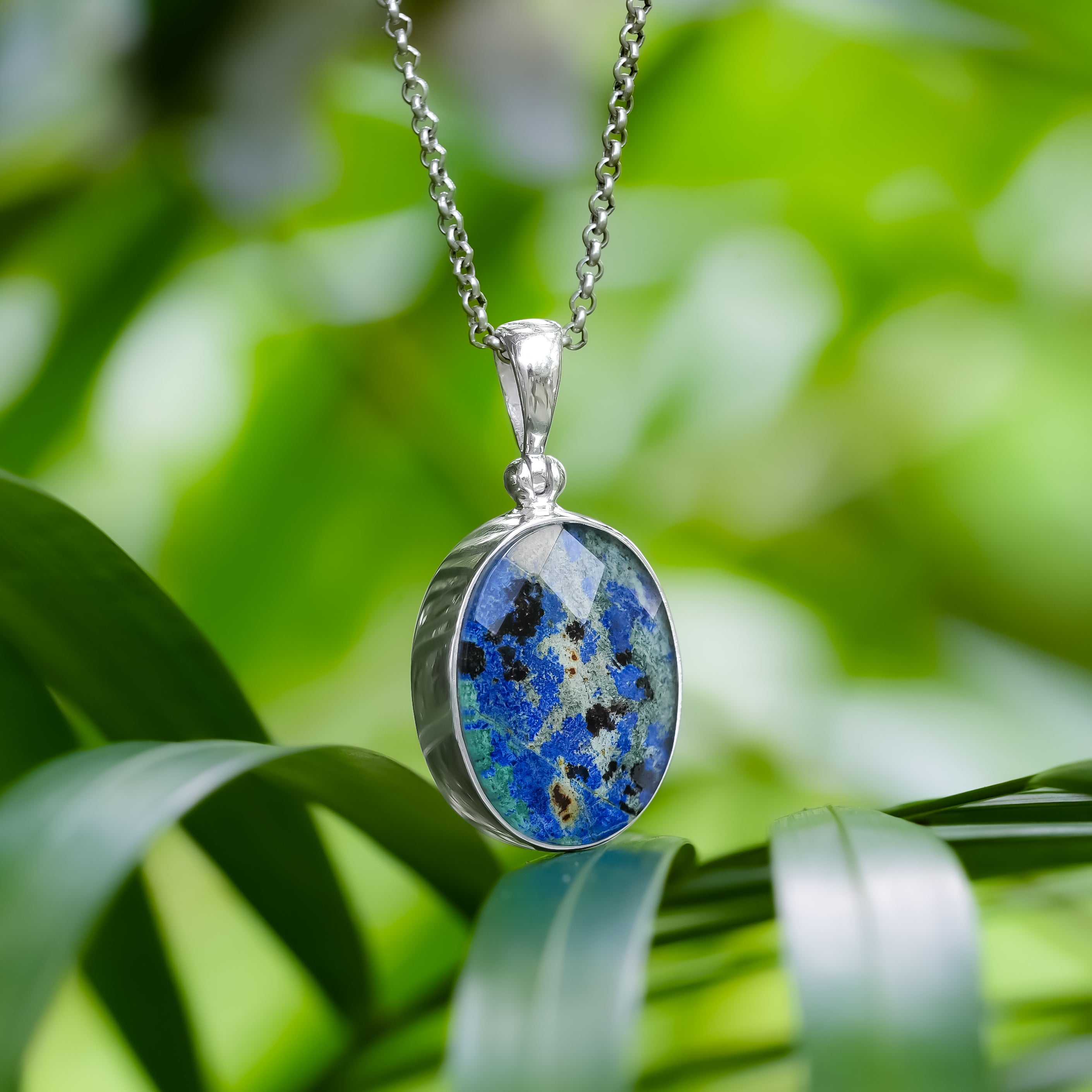 Angled view of a faceted Azurite Malachite oval pendant shown hanging from a chain.