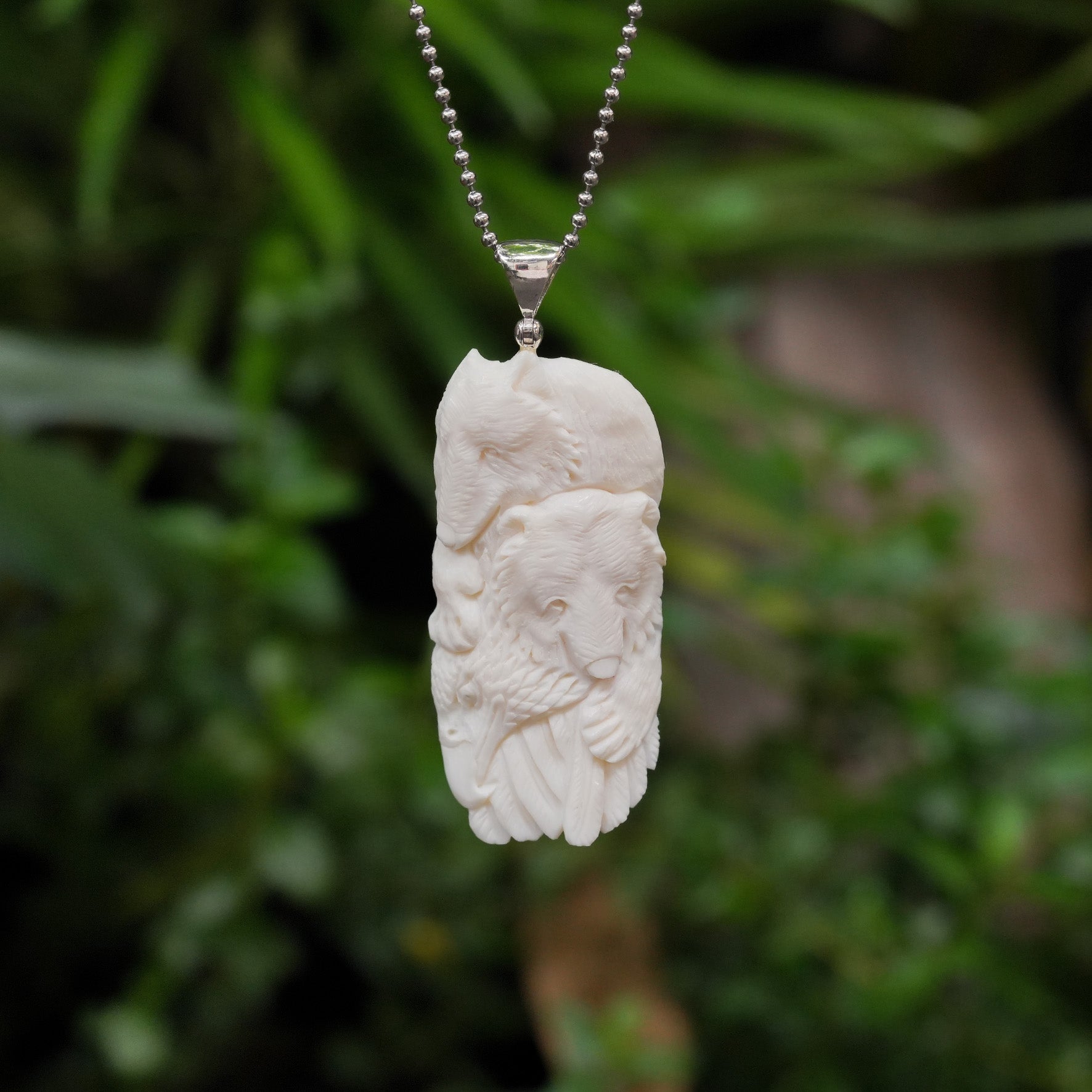 Front-facing view of the same carved buffalo bone eagle, bear, and wolf pendant shown hanging from a chain, displaying the full relief carving and silver bail.
