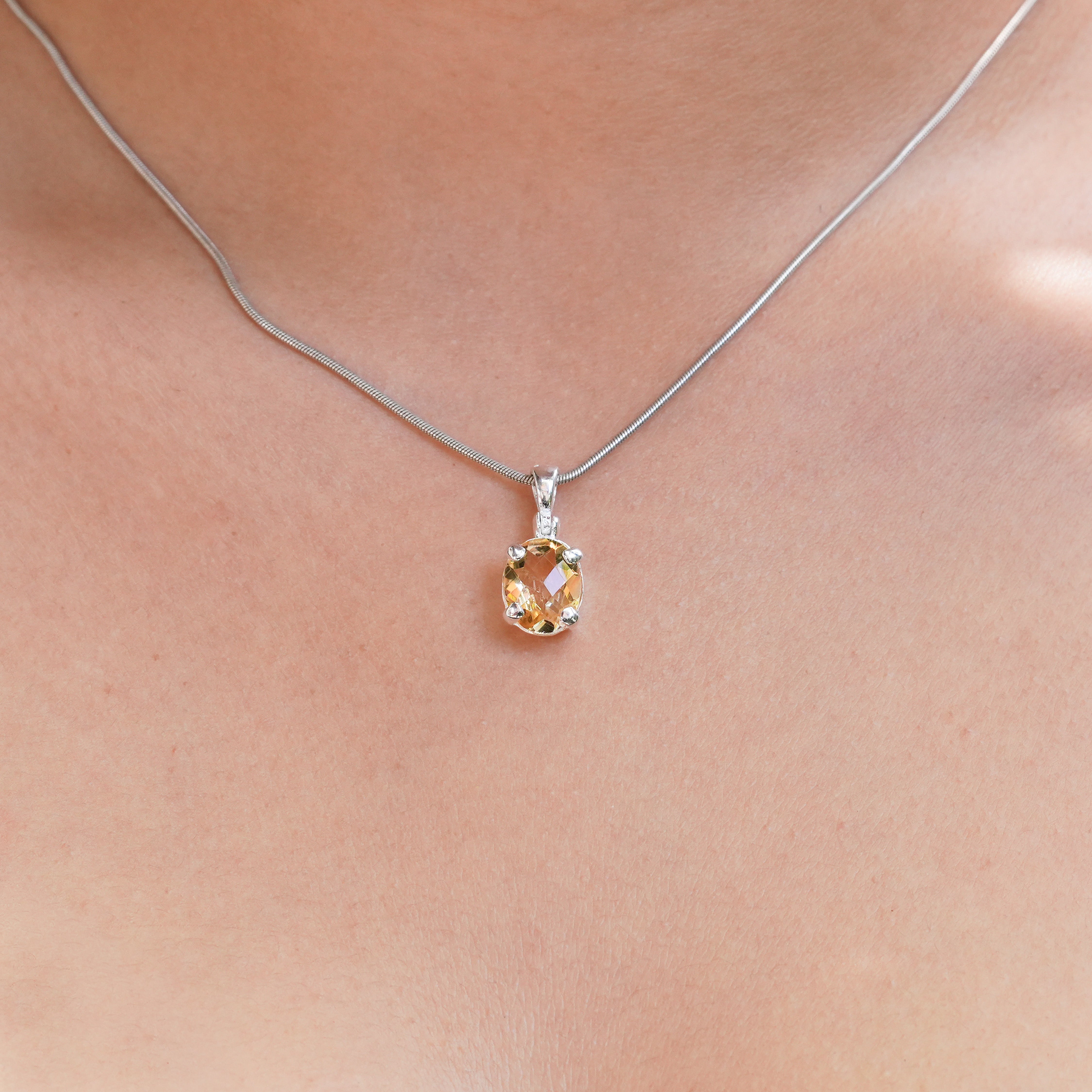 Oval faceted citrine pendant in sterling silver shown worn on a chain around the neck to illustrate scale when worn.
