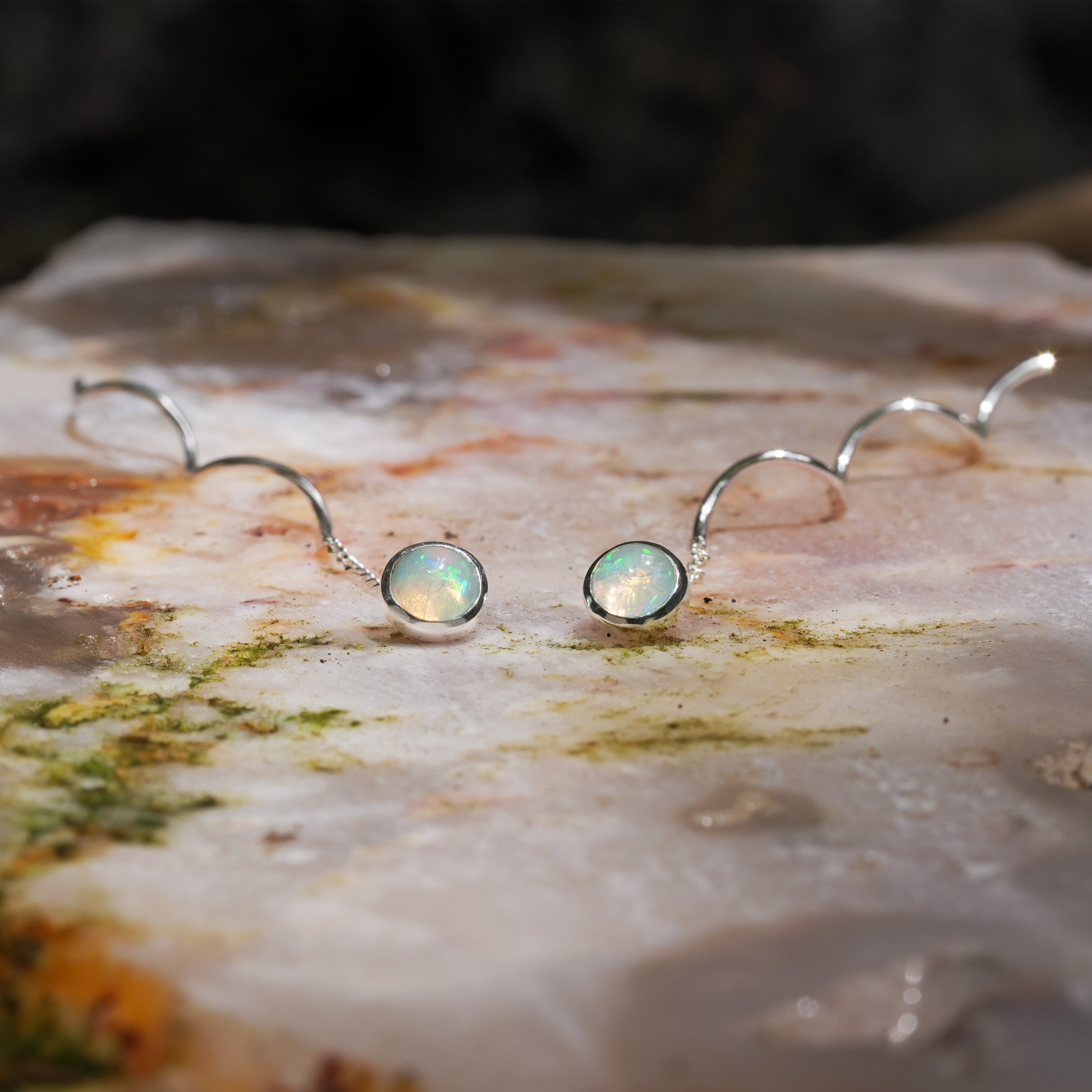 Angled view of round natural ethiopian opal stud earrings with flowing curled wire drop in sterling silver
