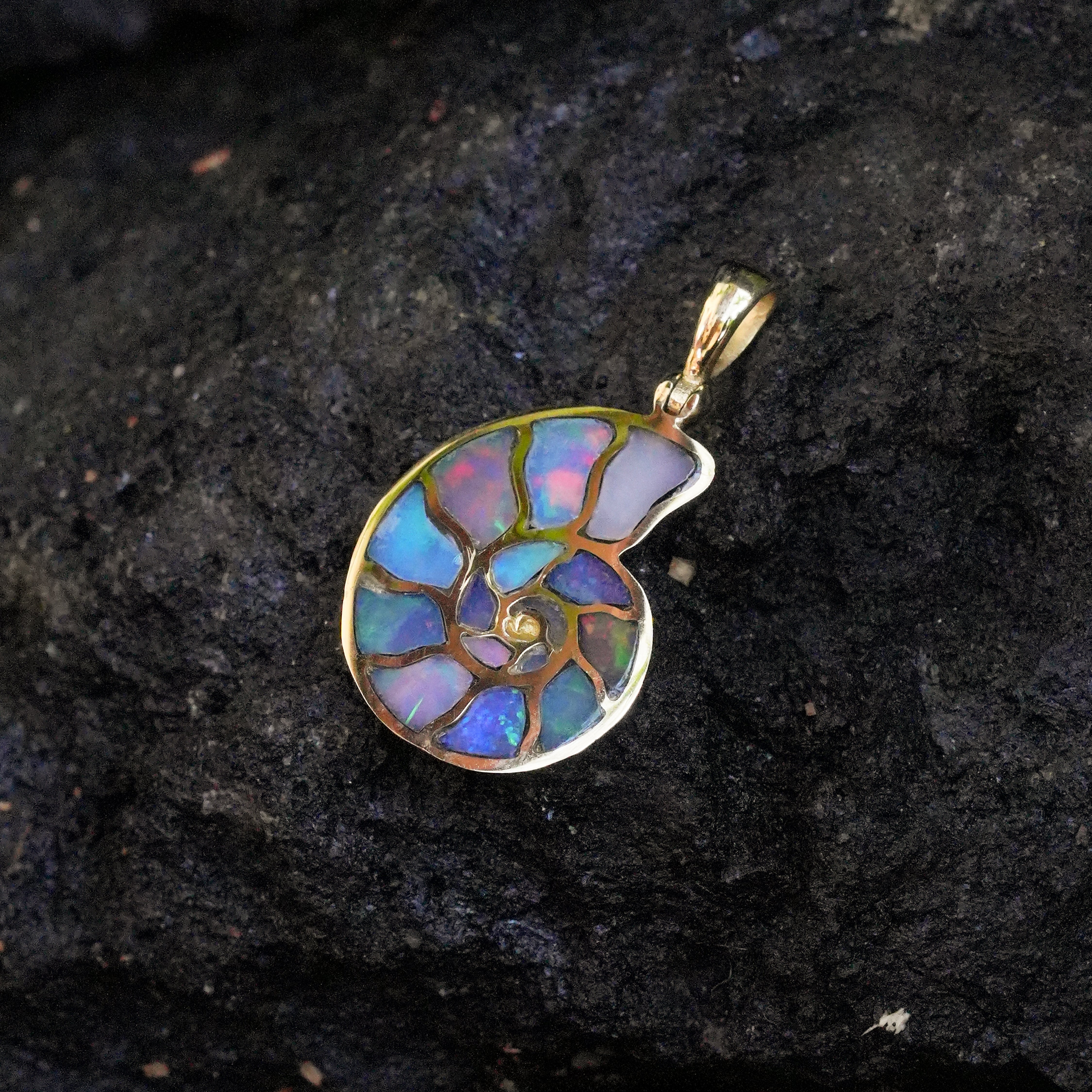 Angled view of a nautilus ammonite pendant with Ethiopian opal inlay showing natural play‑of‑color, set in Nordic gold