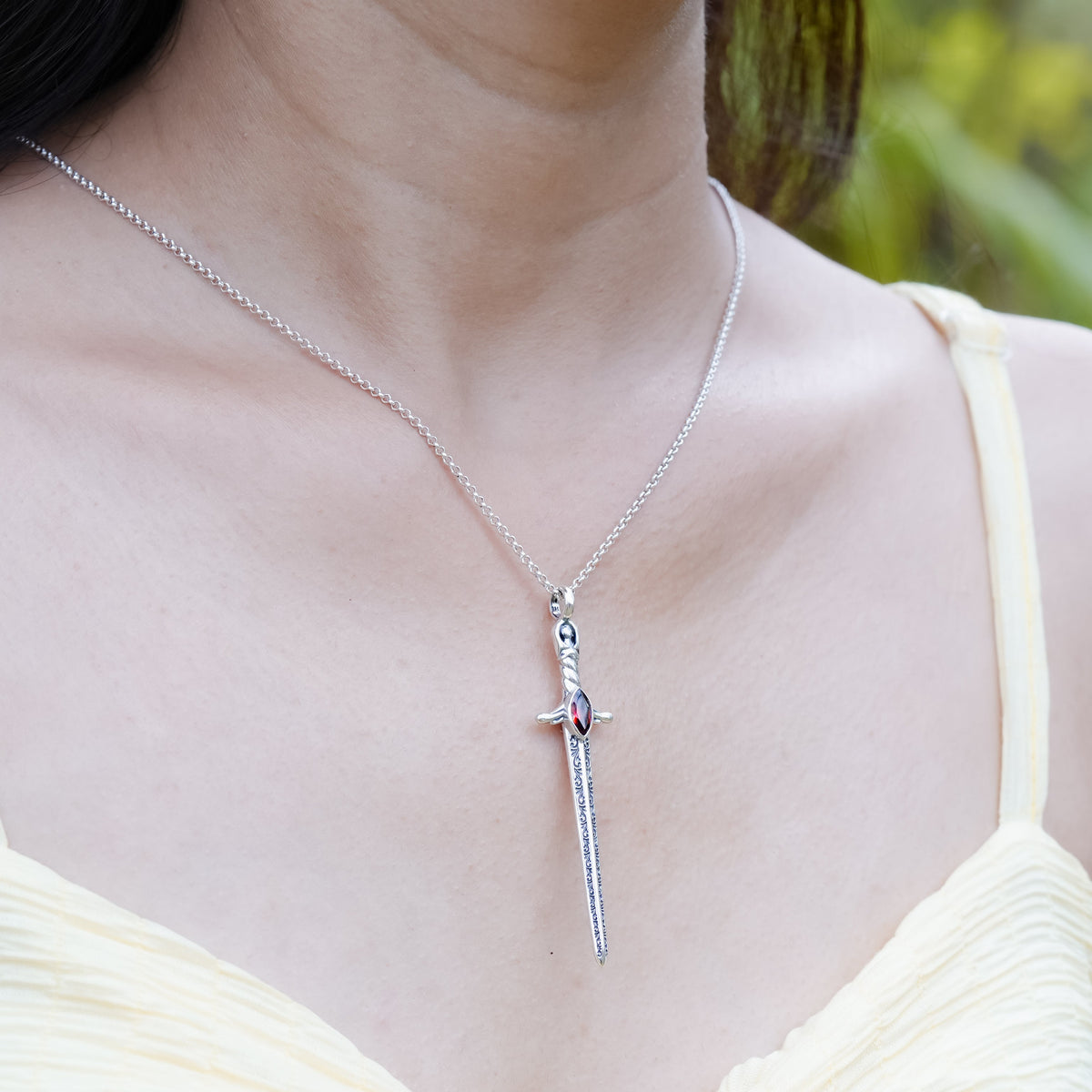 Sterling silver sword pendant necklace with a faceted marquise garnet, worn on a neckline for size reference.