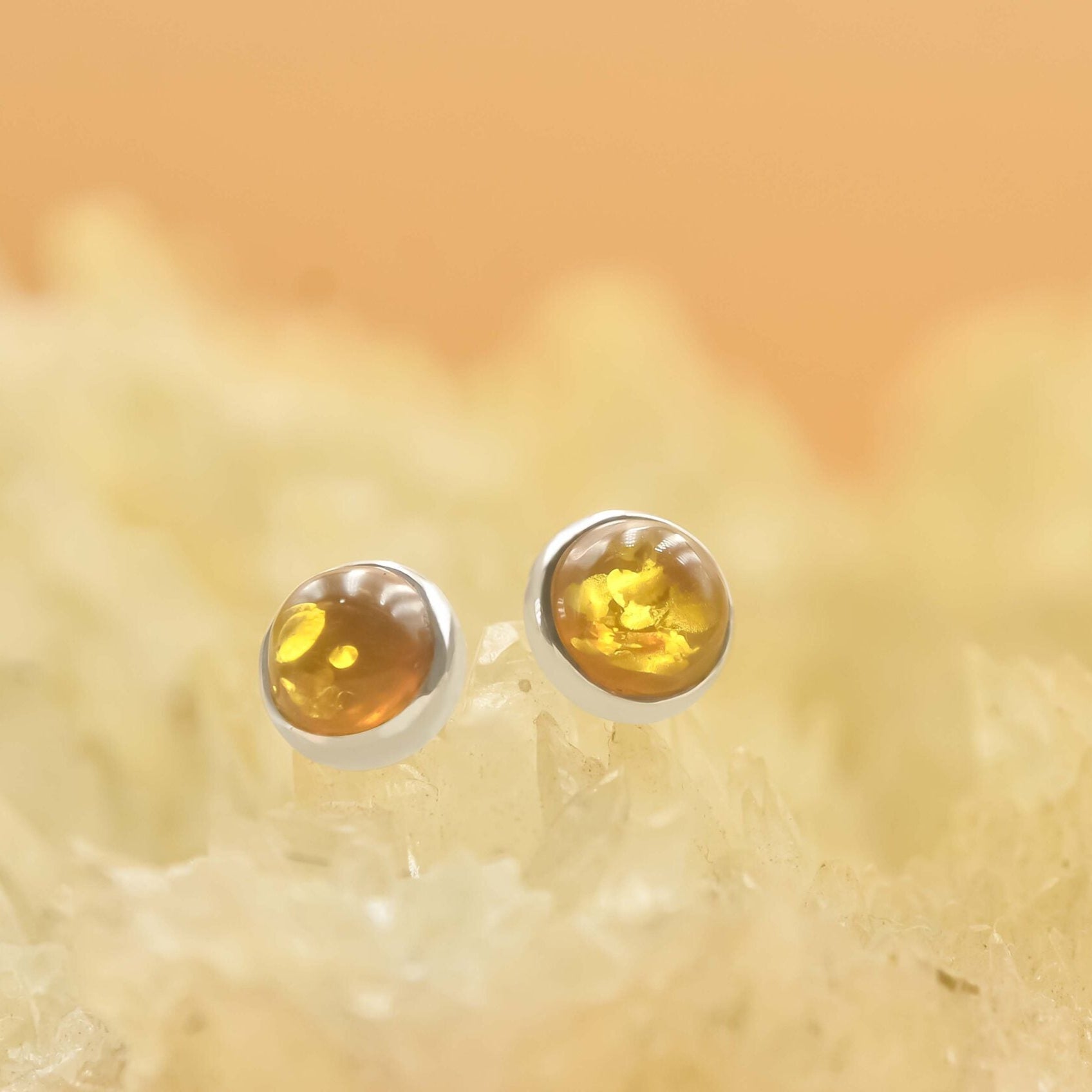 Artistic front view of silver stud earrings featuring round Baltic Amber gemstones with natural inclusions.