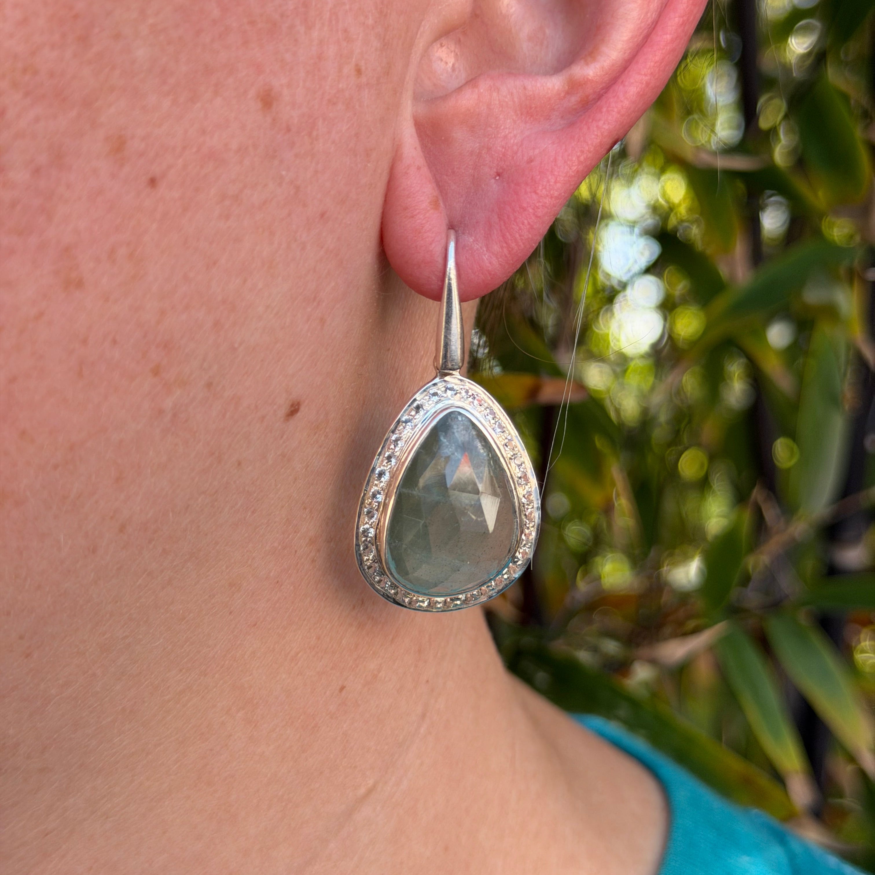 Closeup of Aquamarine faceted angle earrings in sterling silver with a white topaz pave halo