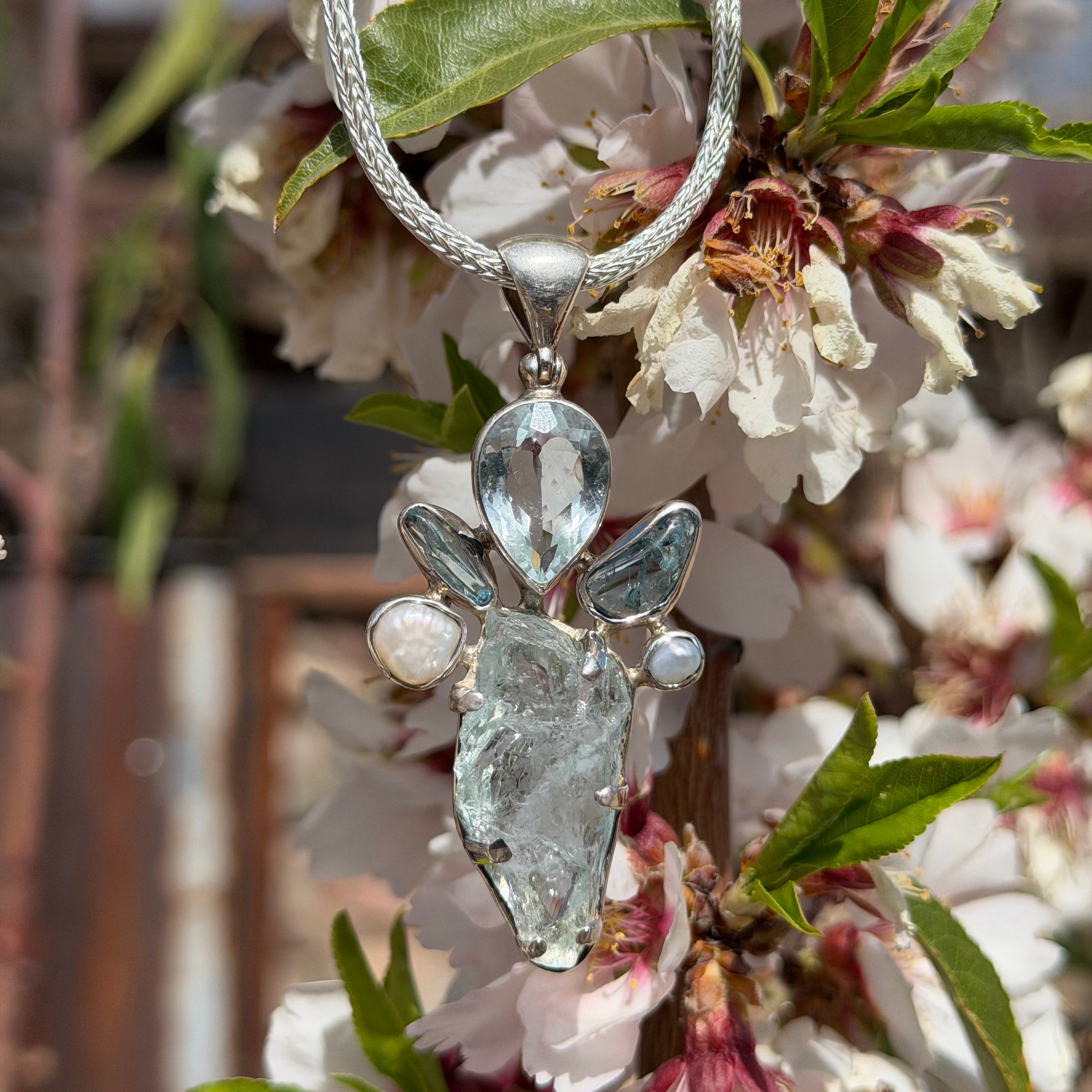 Sterling Silver Aquamarine Pendant with teardrop-shaped facets hanging among cherry blossoms