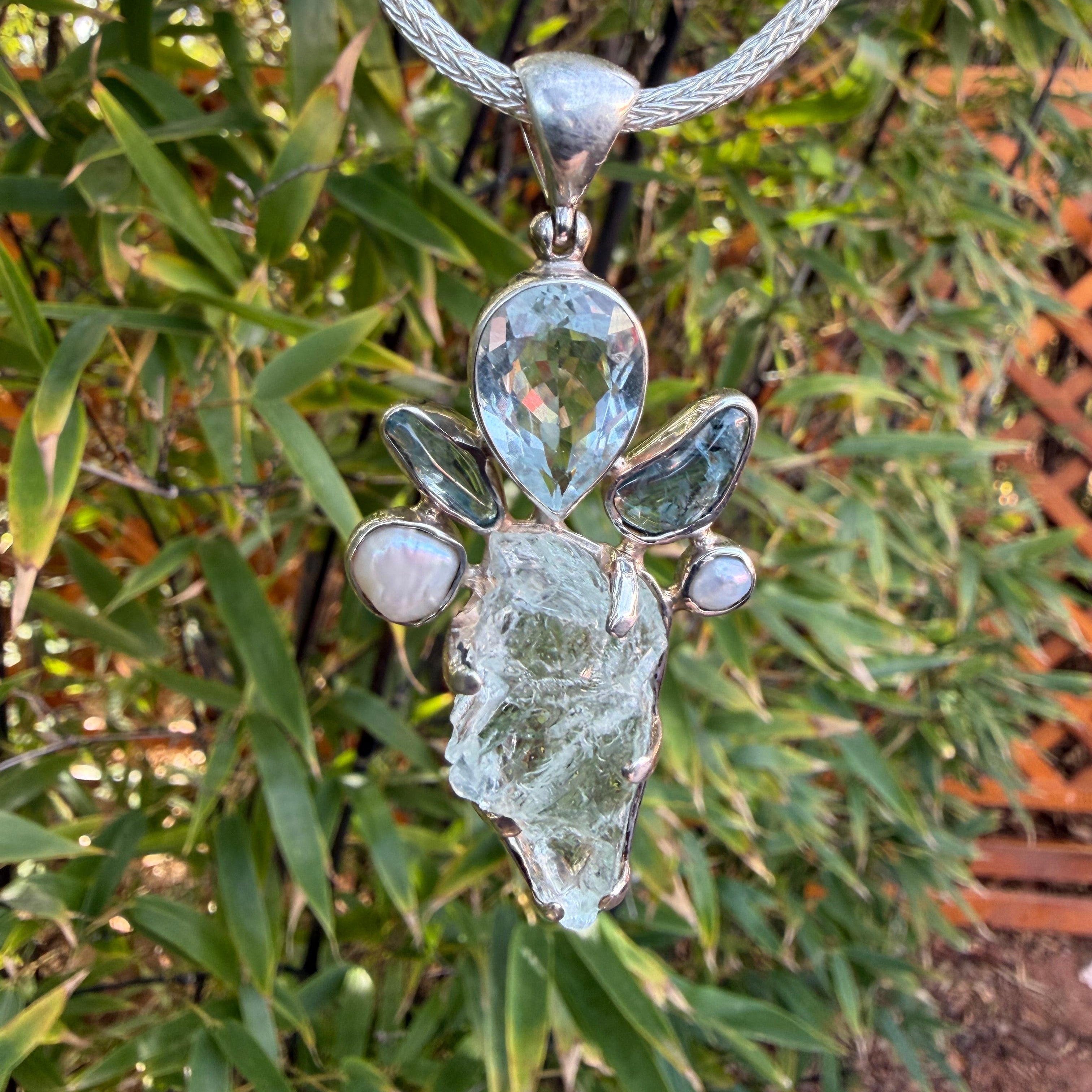 Sterling Silver Aquamarine Pendant with Teardrop Shaped Facet and accent stones against a green leafy background
