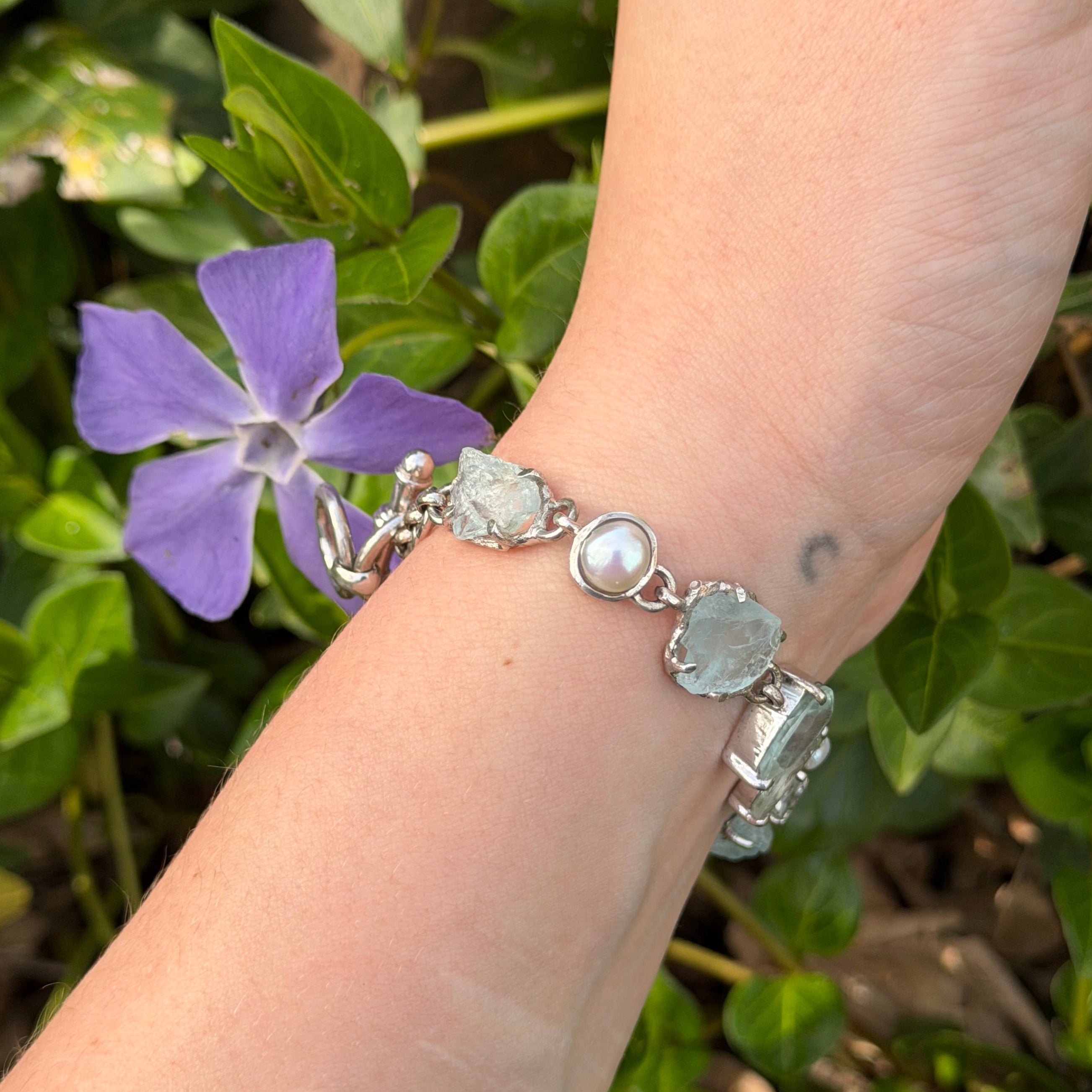 Hand wearing a Sterling silver bracelet with Aquamarine gemstones against a green leafy background