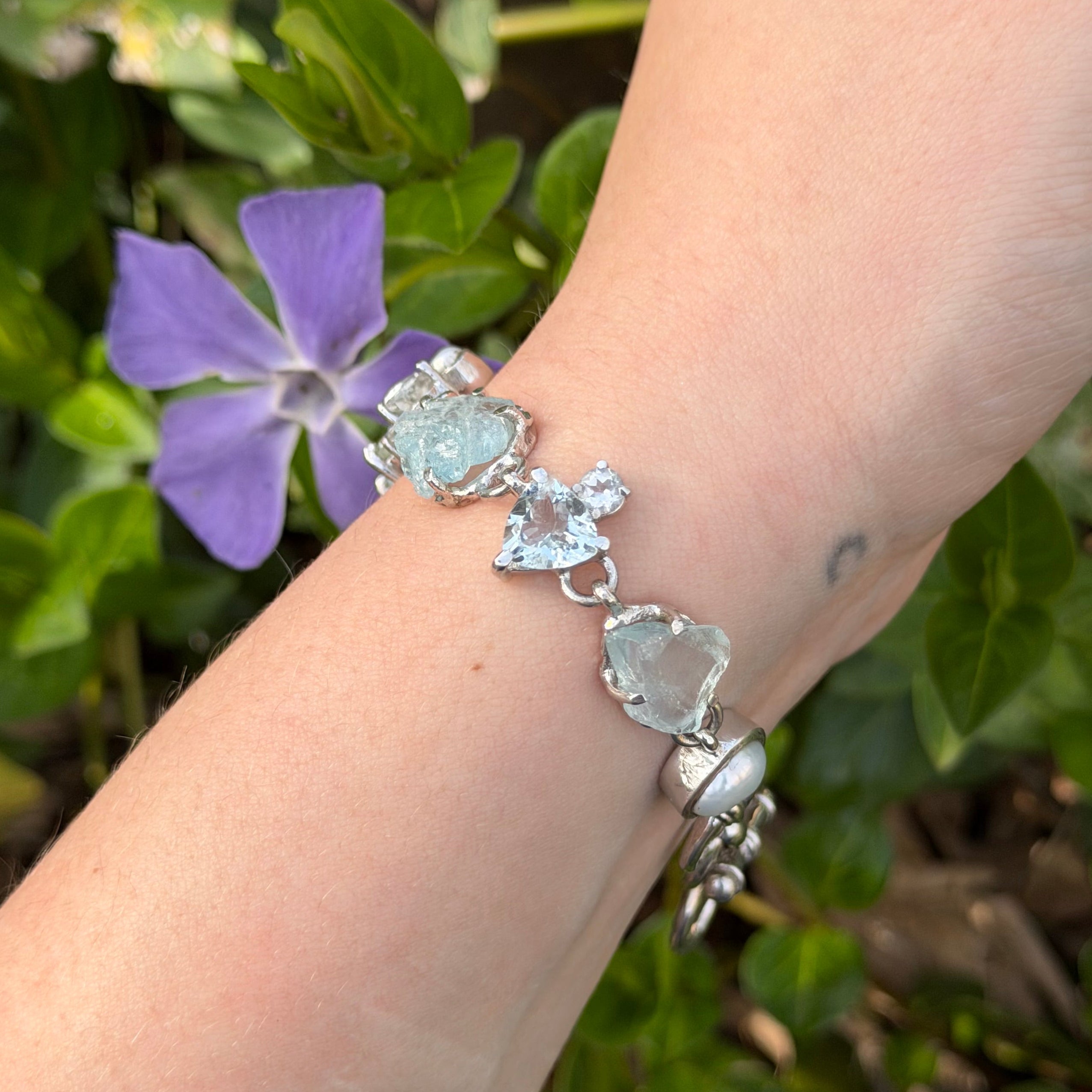 Bracelet with gemstones on a wrist against a natural background with a purple flower.