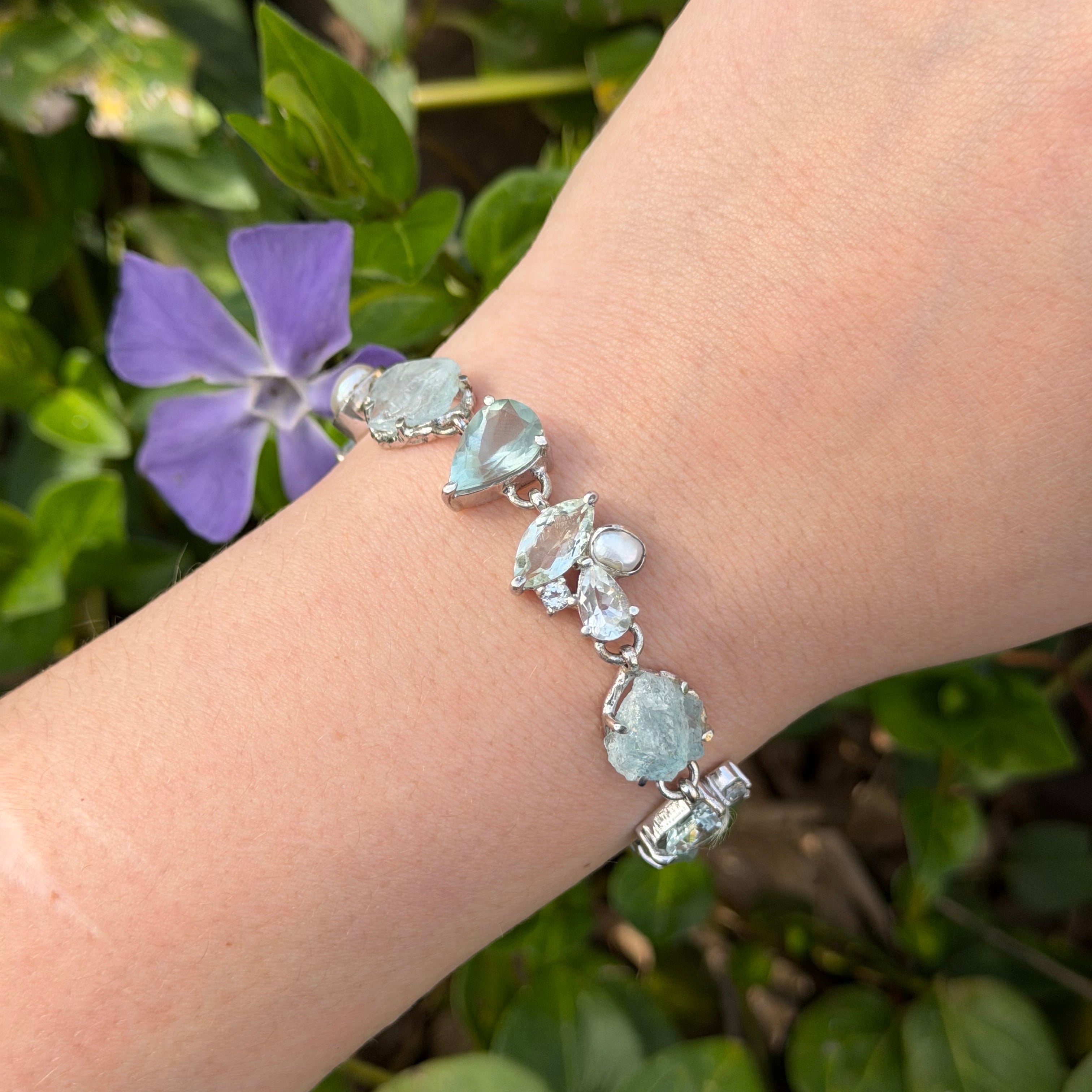 Sterling Silver bracelet with Aquamarine gemstones on a wrist against a natural background with green leaves and a purple flower.