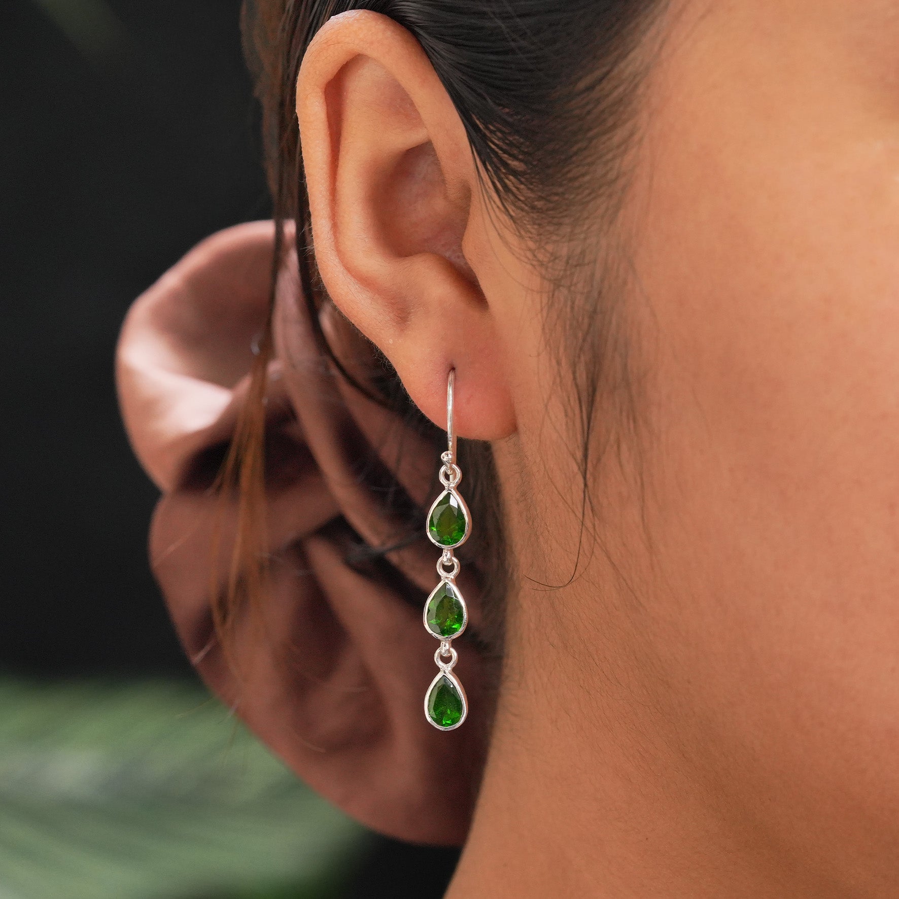 On‑ear image showing the chrome diopside 3‑stone drop earrings worn through the ear, with the three stones cascading downward for scale reference.