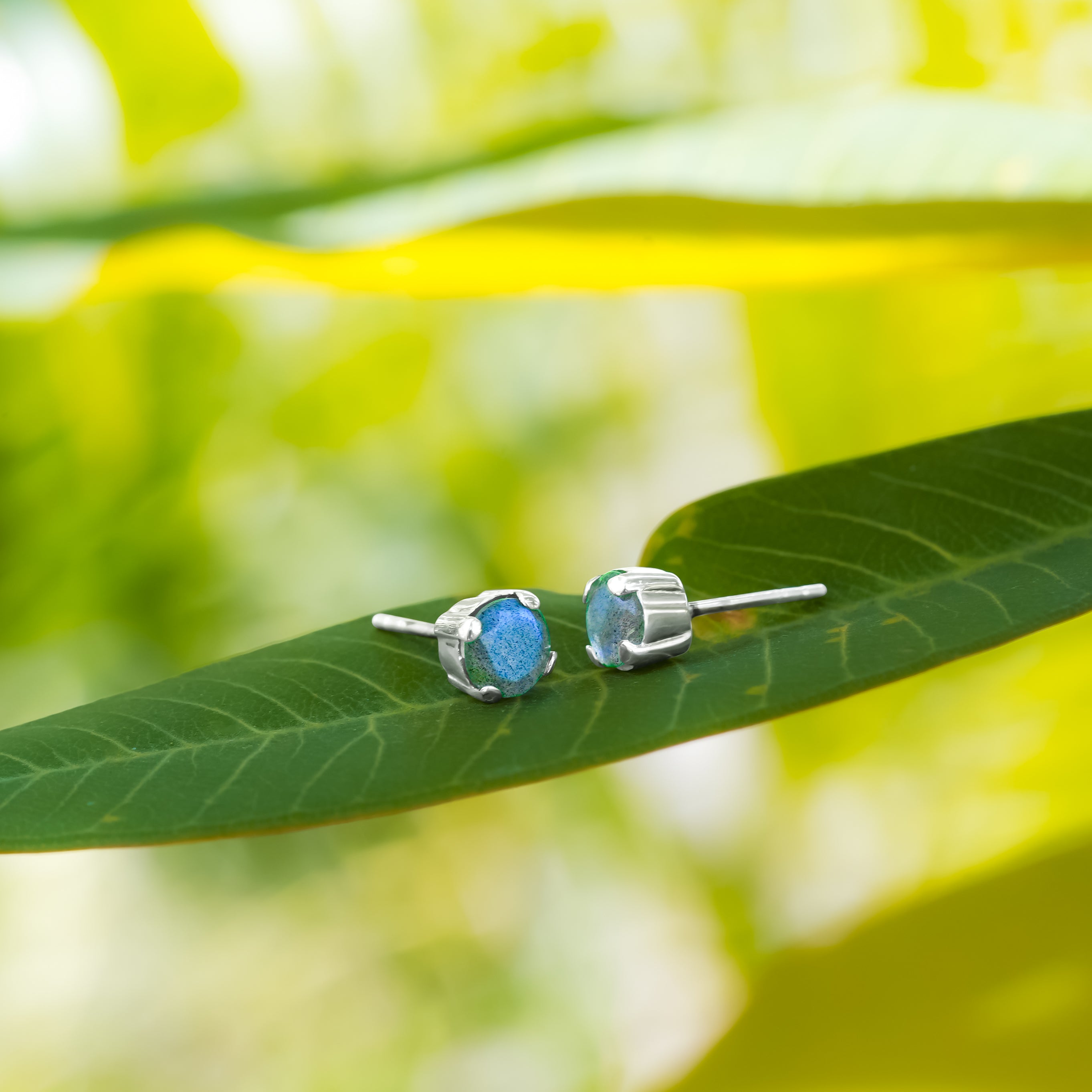 Pair of labradorite stud earrings placed on a leaf surface, showing how the earrings appear in a natural setting with visible blue reflective tones.