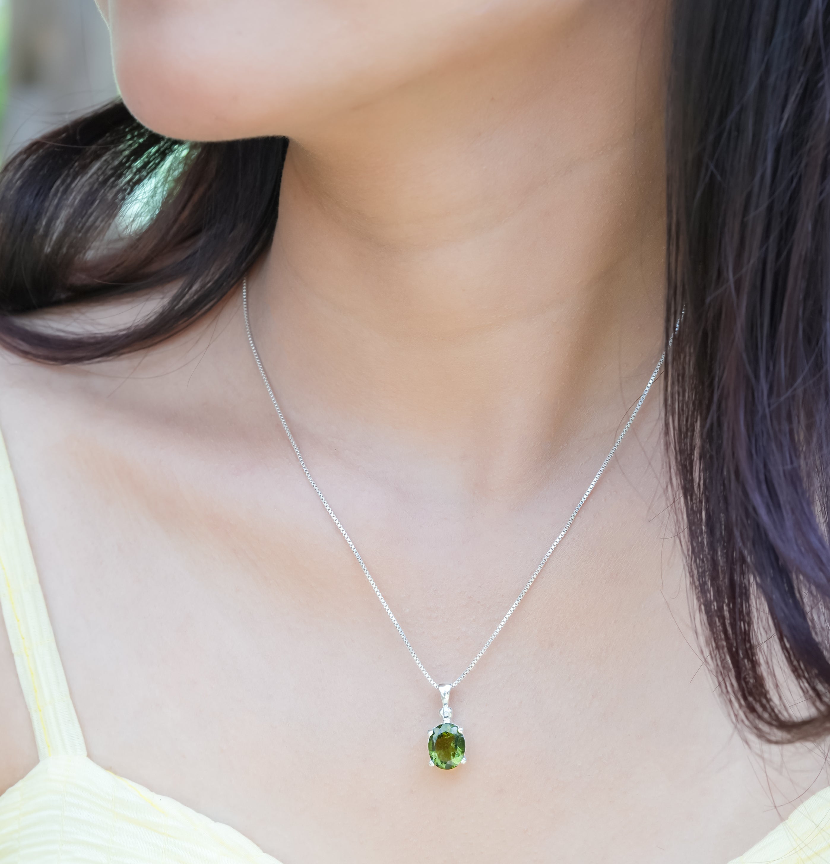 Oval faceted moldavite pendant necklace worn on a neckline, showing size and placement
