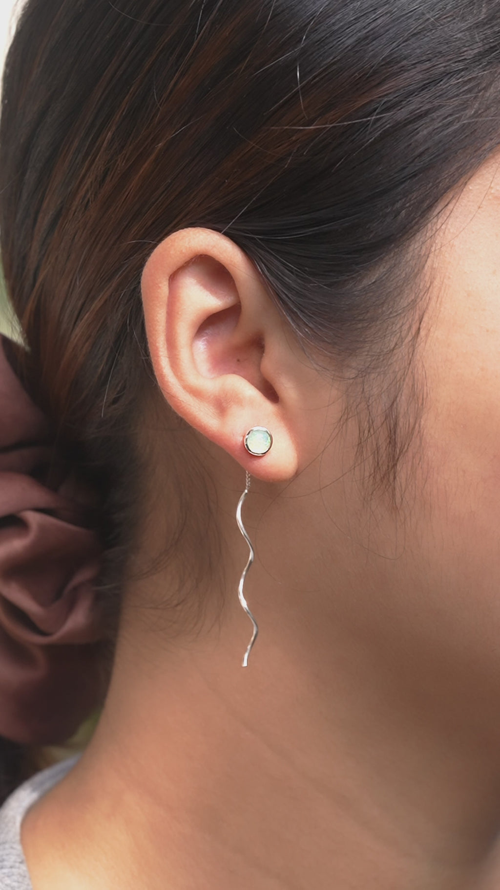 Natural Ethiopian opal stud earrings with flowing curled wire drops worn on ear for size reference. 