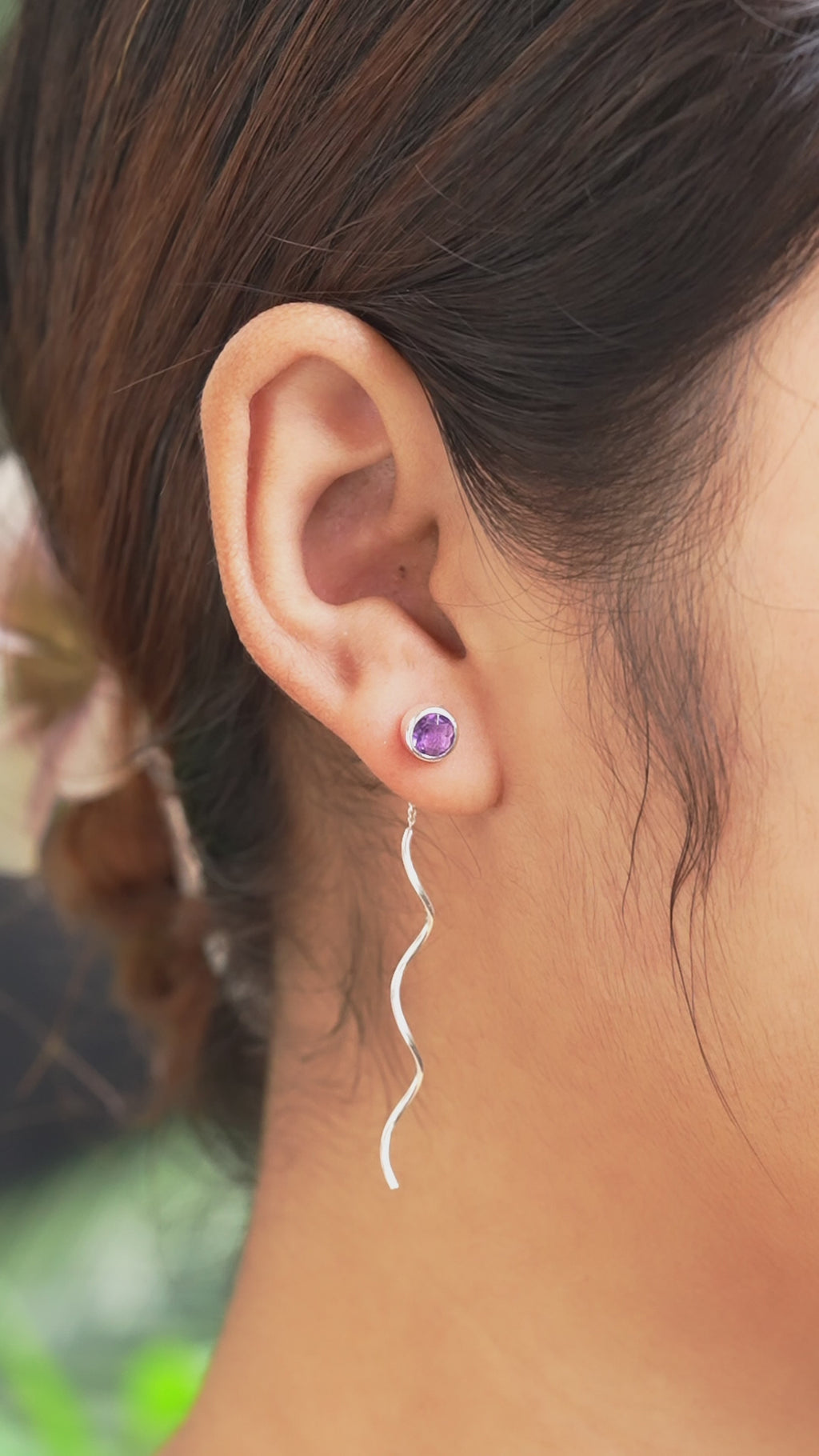 Video showing faceted amethyst stud earrings with flowing curled sterling silver wire drops gently moving while worn on an ear for size reference.