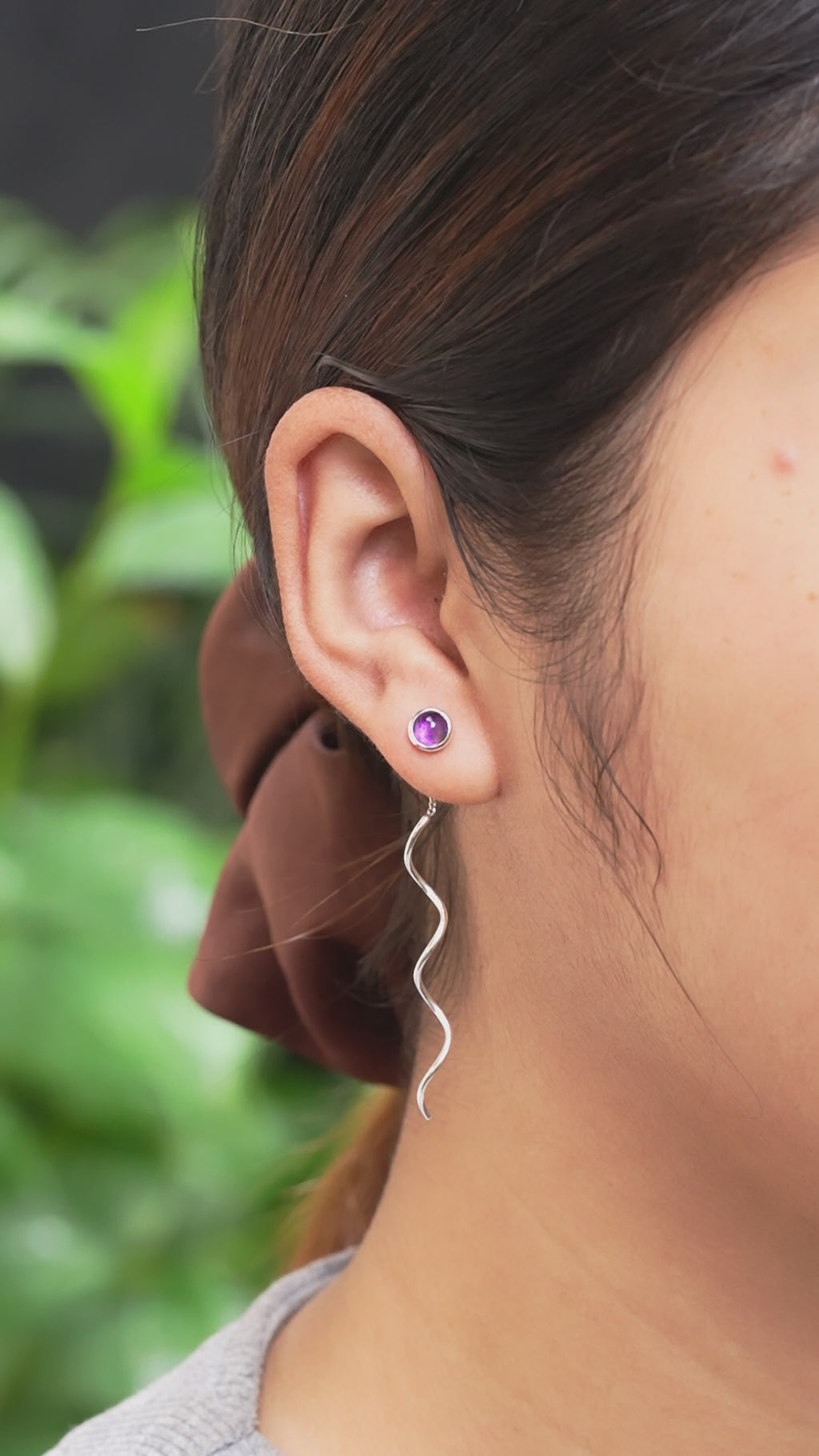 Video showing polished amethyst dangle earrings with flowing curled sterling silver wire drops gently moving while worn on an ear for size reference.