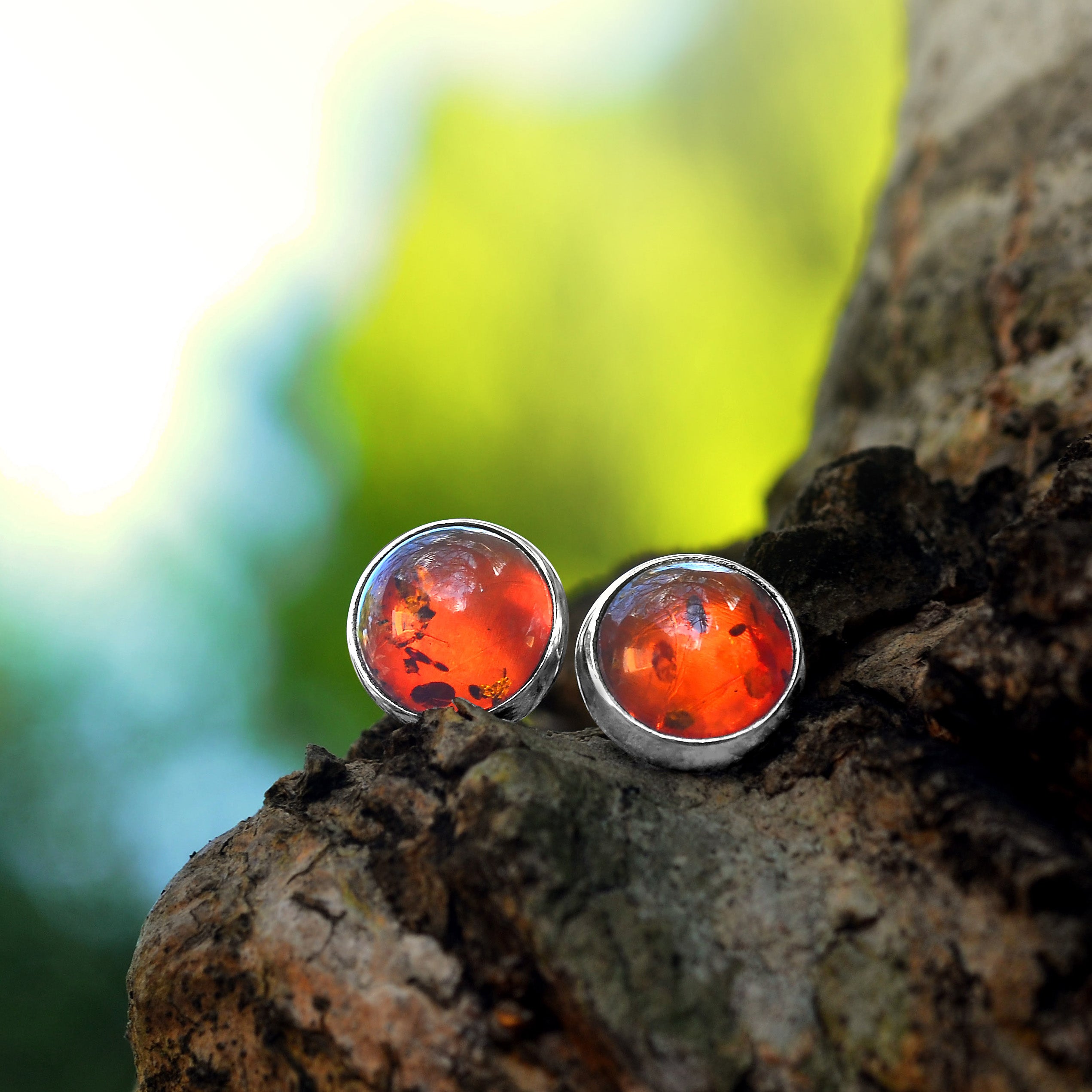 Artistic front view of silver stud earrings featuring round Baltic Amber gemstones with natural inclusions.